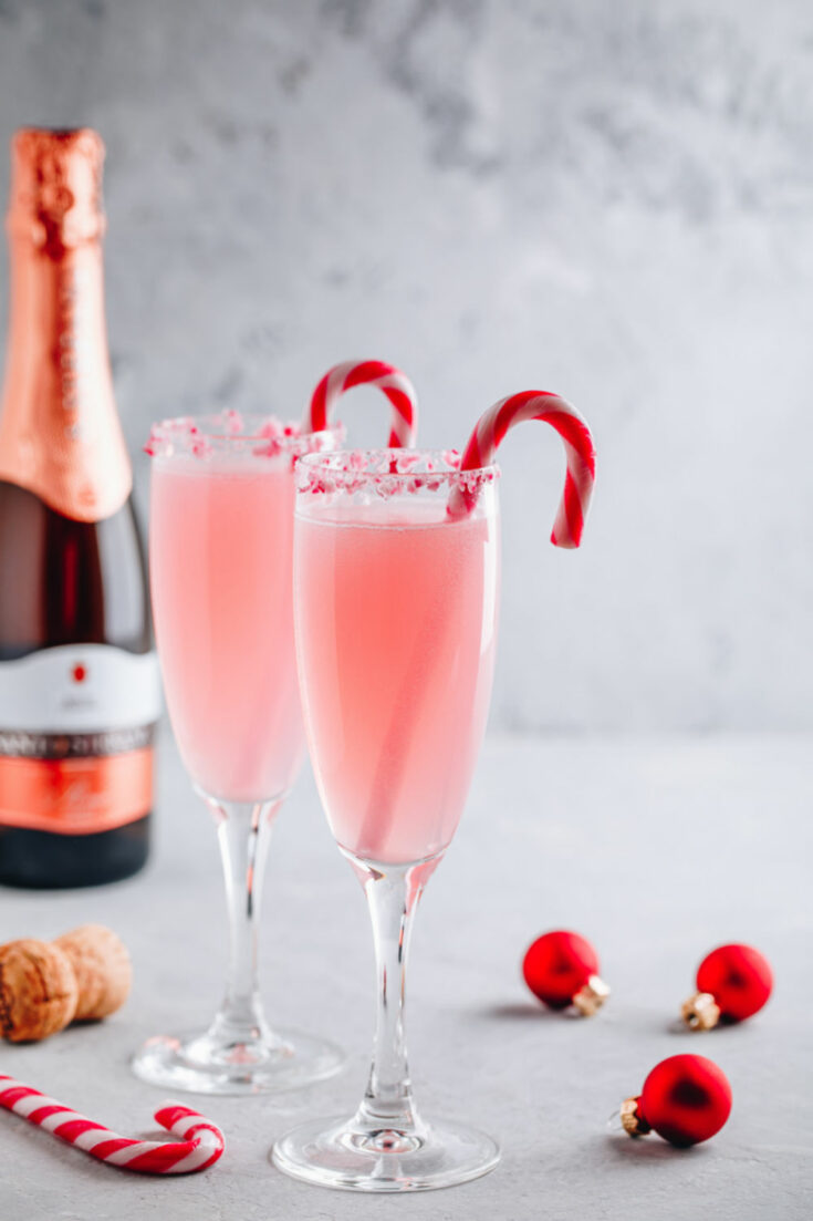 Festive Christmas drink Peppermint Bark Mimosa cocktail with champagne or prosecco and candy cane on gray stone concrete background, copy space.